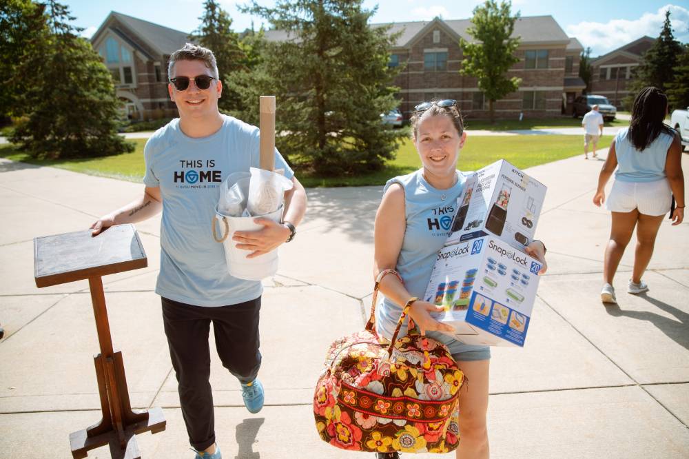 man and woman walking into the dorms with arms full of stuff